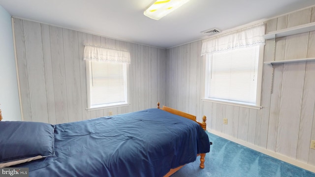 carpeted bedroom featuring multiple windows and wooden walls