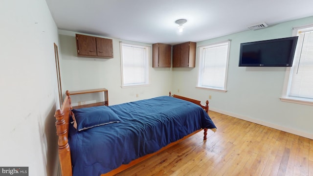 bedroom featuring light wood finished floors, baseboards, multiple windows, and visible vents