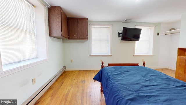 bedroom featuring a baseboard heating unit, multiple windows, light wood-style flooring, and baseboards