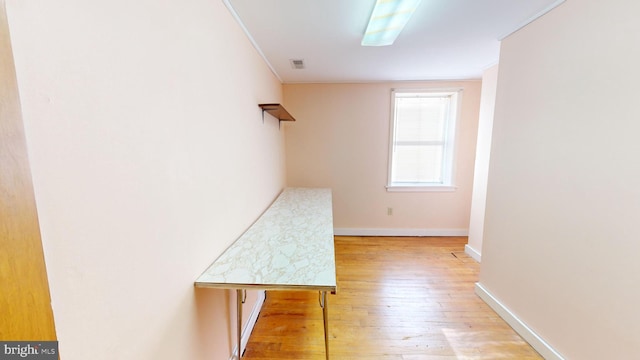 hall with light wood-type flooring, baseboards, visible vents, and crown molding