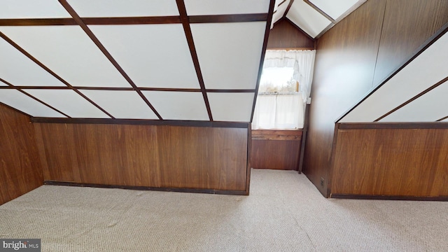 additional living space featuring wooden walls, lofted ceiling with skylight, and light carpet