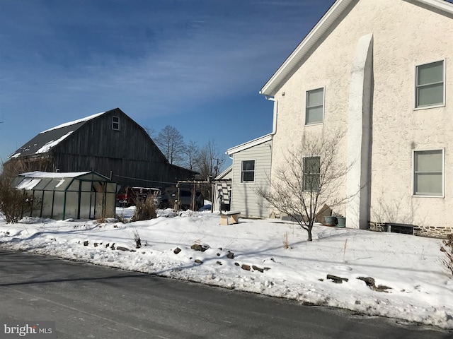 view of snow covered exterior with a barn, an outdoor structure, and stucco siding