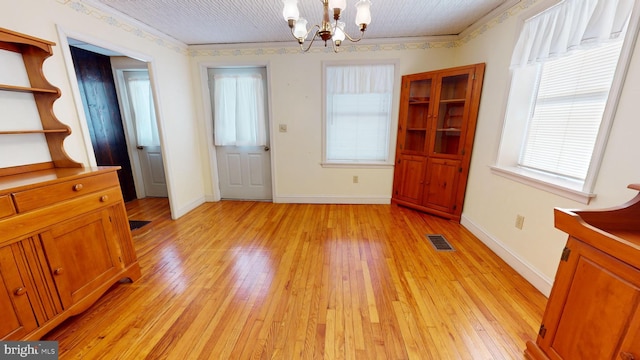 unfurnished dining area with a chandelier, visible vents, baseboards, light wood-type flooring, and crown molding