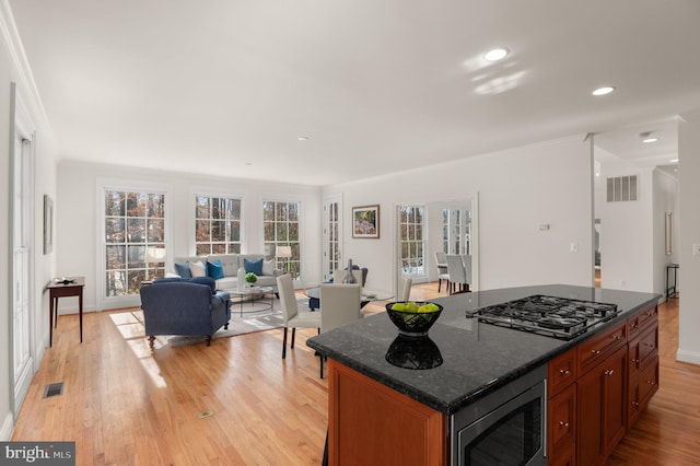 kitchen featuring crown molding, light hardwood / wood-style flooring, dark stone countertops, appliances with stainless steel finishes, and a kitchen island