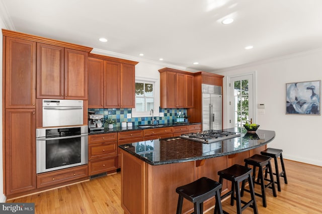 kitchen with a kitchen bar, tasteful backsplash, a center island, light wood-type flooring, and appliances with stainless steel finishes