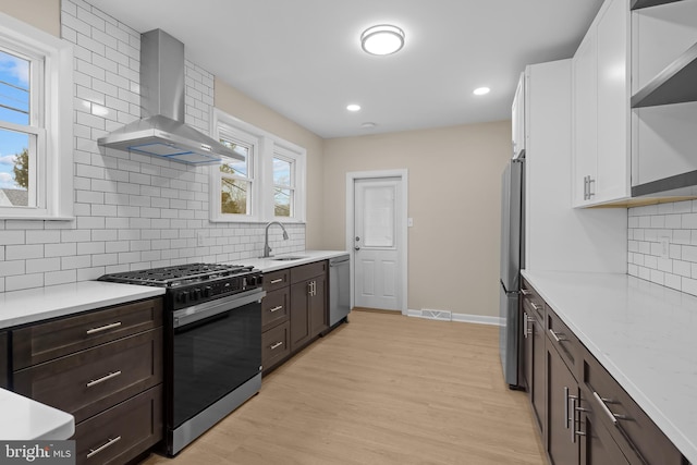 kitchen featuring white cabinets, dark brown cabinetry, wall chimney range hood, stainless steel appliances, and sink