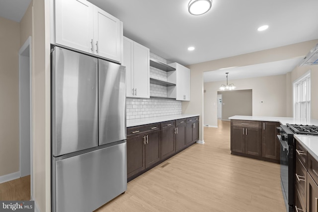 kitchen featuring backsplash, pendant lighting, stainless steel refrigerator, black range with gas stovetop, and white cabinets