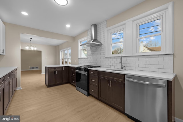 kitchen with gas stove, wall chimney range hood, pendant lighting, stainless steel dishwasher, and sink