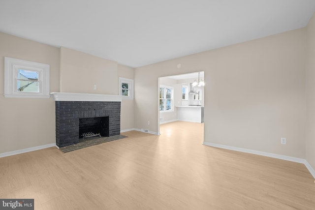 unfurnished living room with a fireplace, plenty of natural light, a chandelier, and light hardwood / wood-style flooring