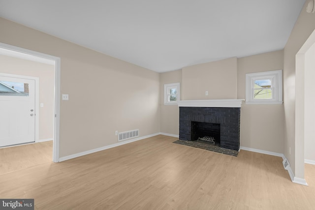 unfurnished living room with a brick fireplace and light hardwood / wood-style flooring