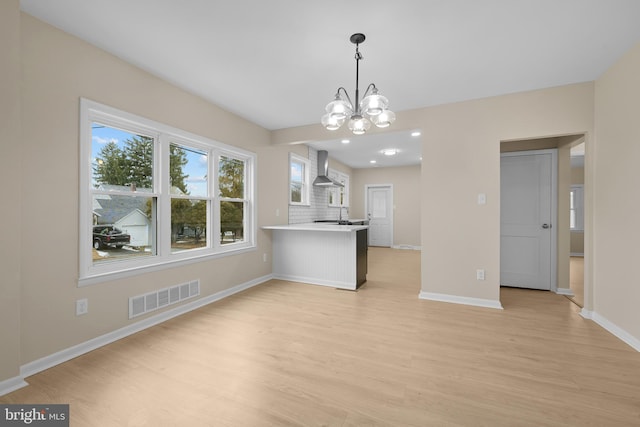 kitchen with light hardwood / wood-style floors, a chandelier, kitchen peninsula, and wall chimney exhaust hood