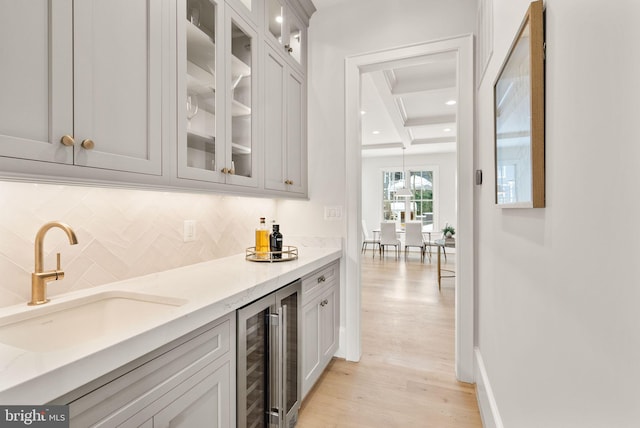 bar with decorative backsplash, light stone counters, beverage cooler, sink, and light hardwood / wood-style flooring