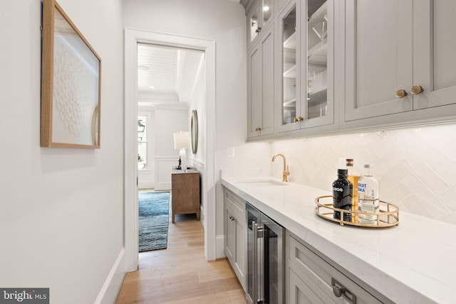 bar with light wood-type flooring, light stone counters, beverage cooler, sink, and gray cabinets