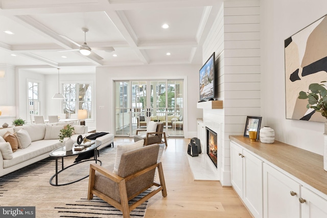 living room with coffered ceiling, a large fireplace, ceiling fan, beam ceiling, and light hardwood / wood-style flooring