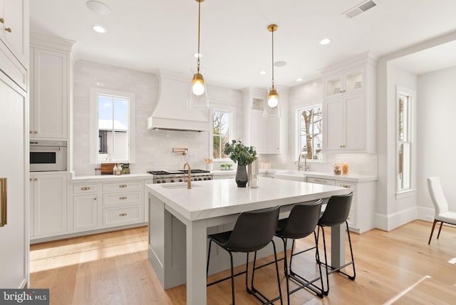 kitchen featuring white cabinetry, a kitchen island with sink, light hardwood / wood-style floors, and custom exhaust hood