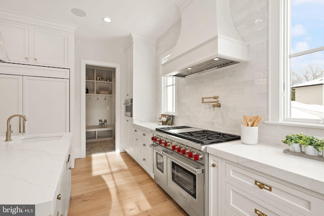 kitchen featuring light stone counters, white cabinets, stainless steel appliances, and custom exhaust hood