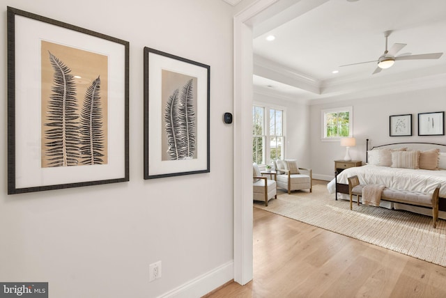 bedroom featuring ceiling fan, light hardwood / wood-style floors, crown molding, and a tray ceiling