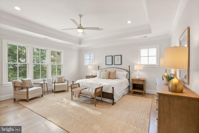 bedroom featuring ceiling fan, a raised ceiling, light wood-type flooring, and multiple windows