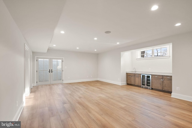 unfurnished living room featuring wet bar, light wood-type flooring, beverage cooler, and french doors