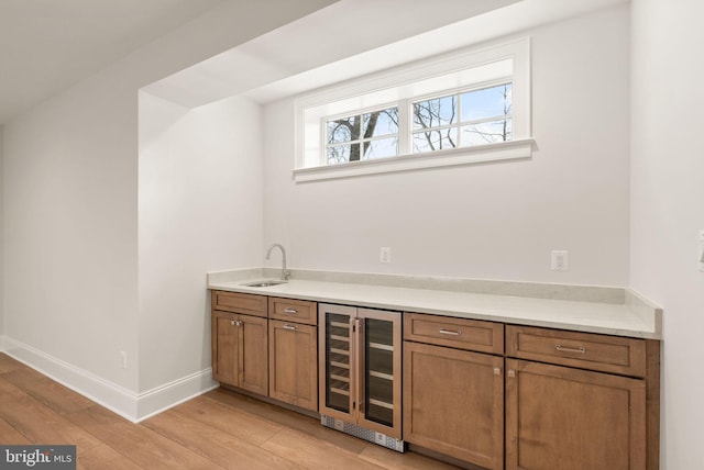 bar featuring sink, beverage cooler, and light hardwood / wood-style flooring