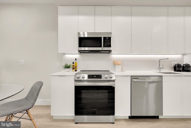 kitchen featuring white cabinets, appliances with stainless steel finishes, light wood-type flooring, and sink