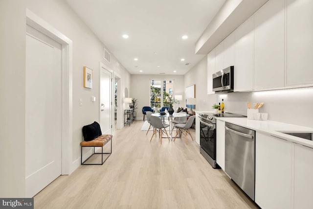 kitchen with white cabinets, stainless steel appliances, and light hardwood / wood-style flooring