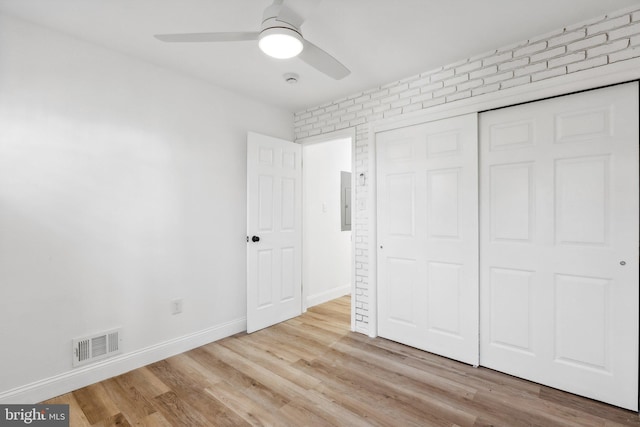 unfurnished bedroom featuring brick wall, light hardwood / wood-style floors, a closet, and ceiling fan