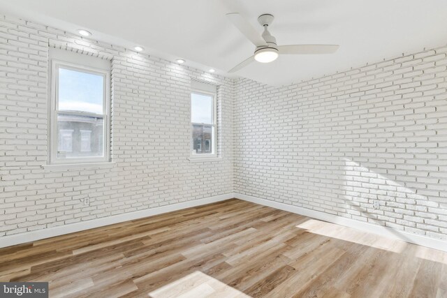 unfurnished room featuring ceiling fan, brick wall, and light wood-type flooring