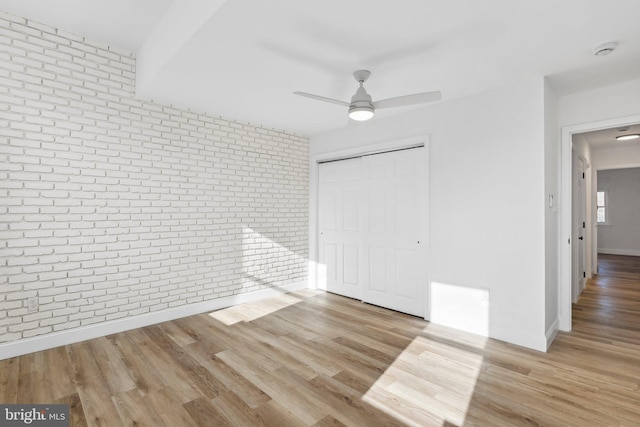 unfurnished bedroom featuring ceiling fan, light wood-type flooring, brick wall, and a closet