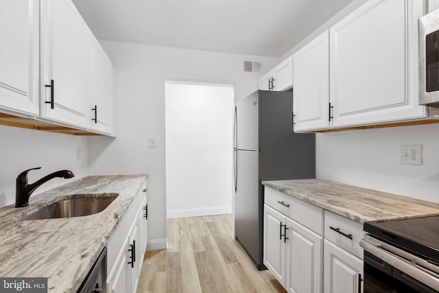 kitchen with white cabinets, light hardwood / wood-style floors, light stone counters, and sink