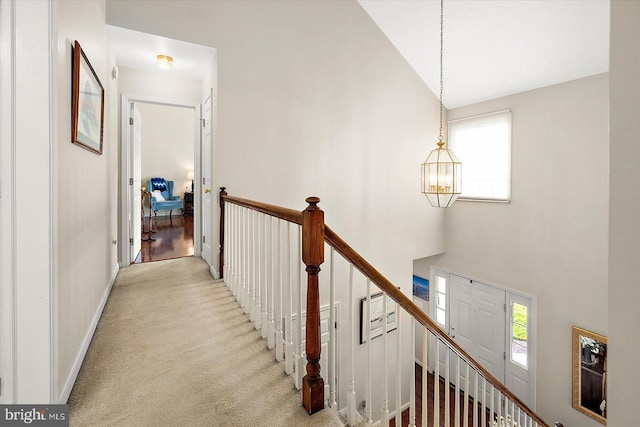 hall with light colored carpet, high vaulted ceiling, and a chandelier