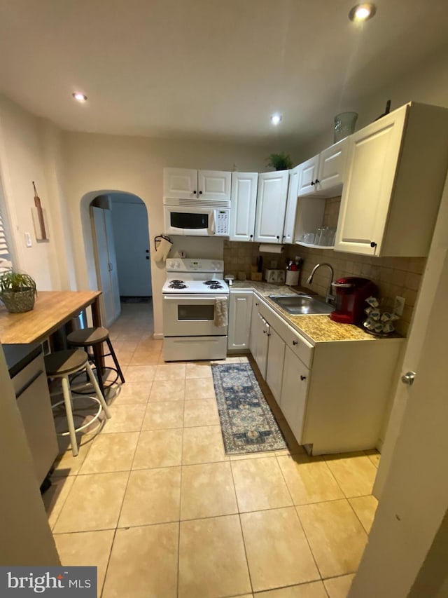 kitchen featuring decorative backsplash, white appliances, sink, white cabinetry, and light tile patterned flooring