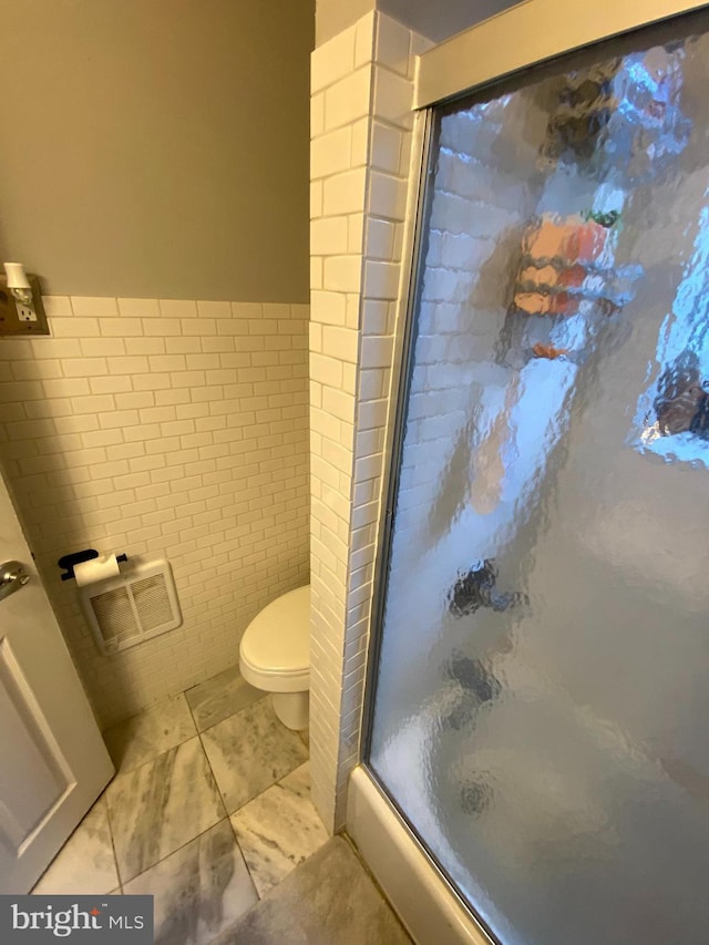 bathroom with an enclosed shower, toilet, and tile walls