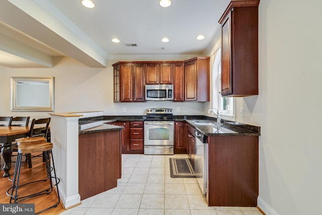 kitchen with appliances with stainless steel finishes, ornamental molding, sink, light tile patterned floors, and dark stone countertops