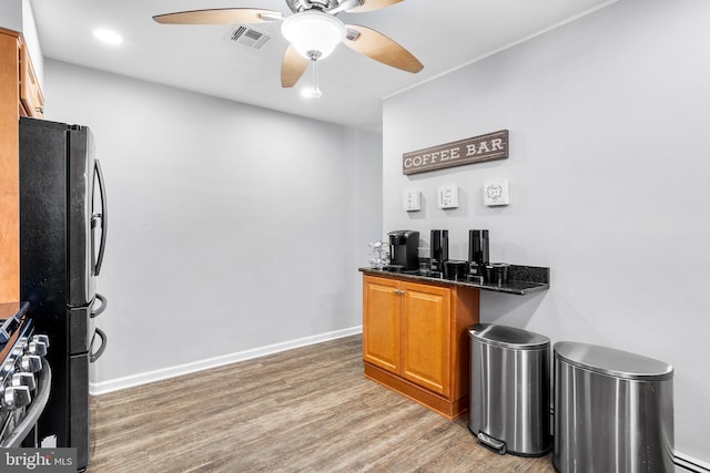 bar featuring hardwood / wood-style floors, black fridge, ceiling fan, dark stone countertops, and stainless steel range