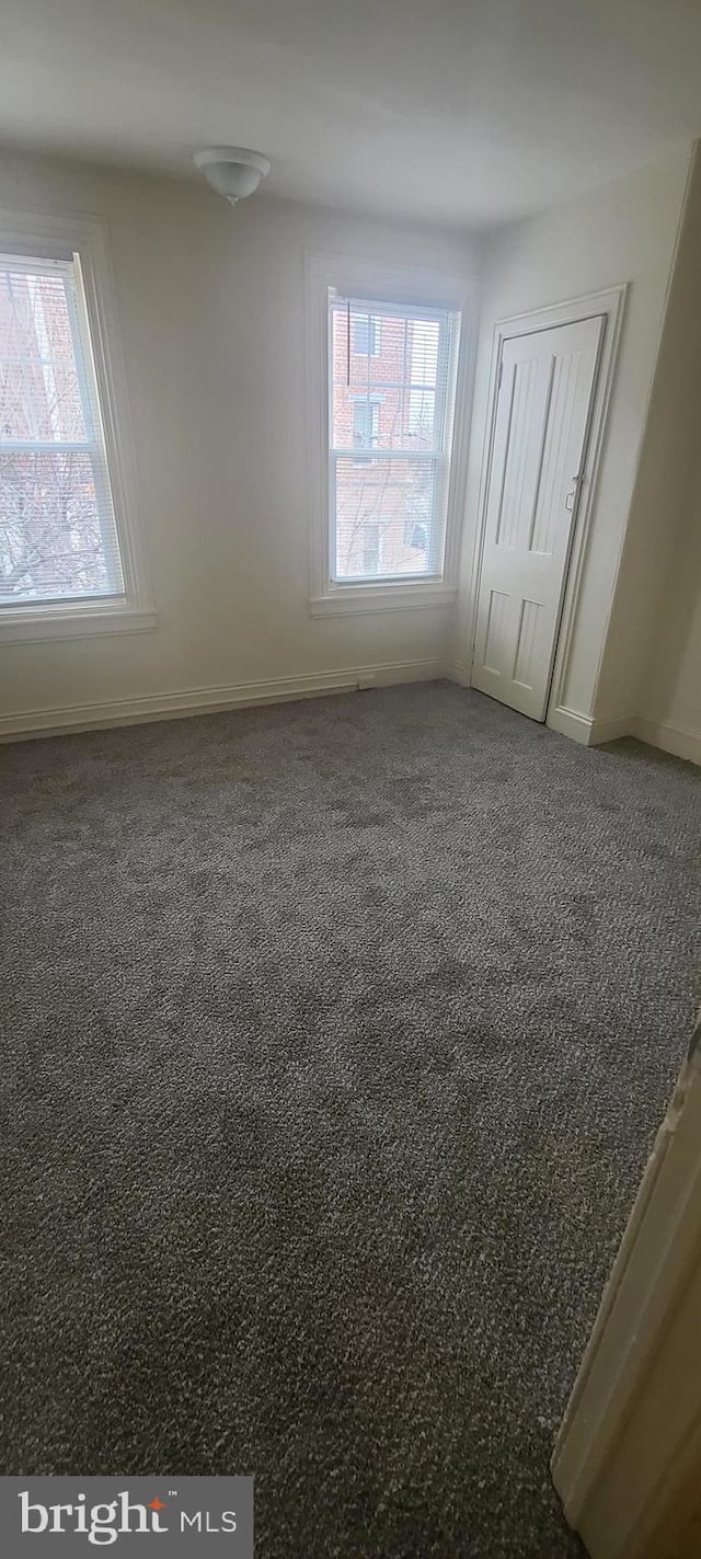 unfurnished bedroom with dark colored carpet, a closet, and multiple windows