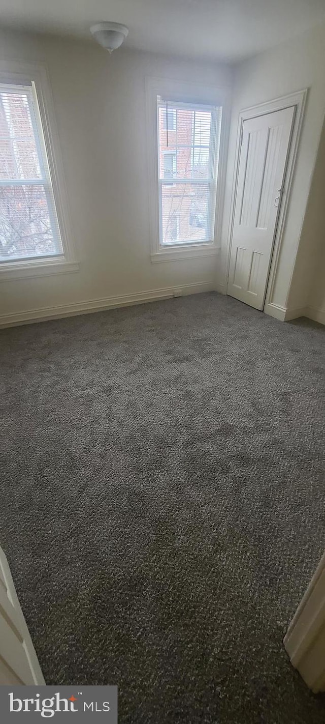 unfurnished bedroom with dark carpet, a closet, and multiple windows