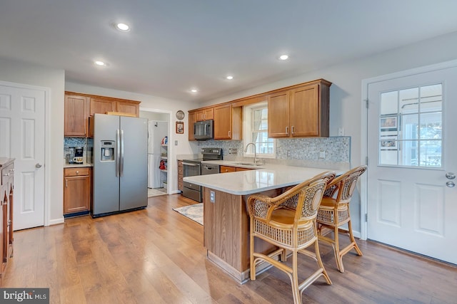 kitchen featuring kitchen peninsula, appliances with stainless steel finishes, a kitchen bar, sink, and light hardwood / wood-style flooring