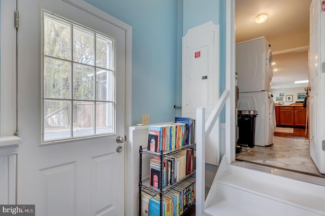 doorway to outside with electric panel and stacked washer and clothes dryer