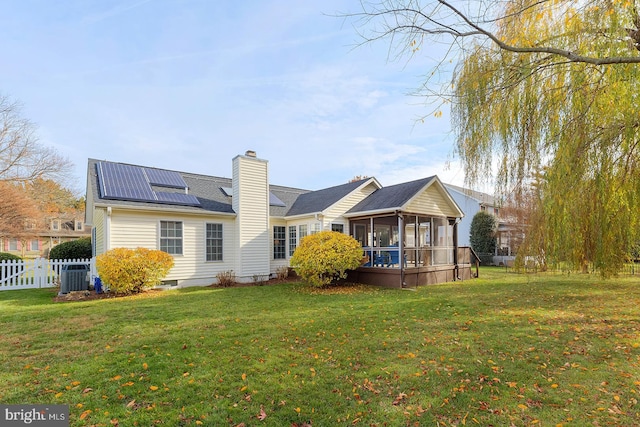 back of house with a lawn, central AC, a sunroom, and solar panels