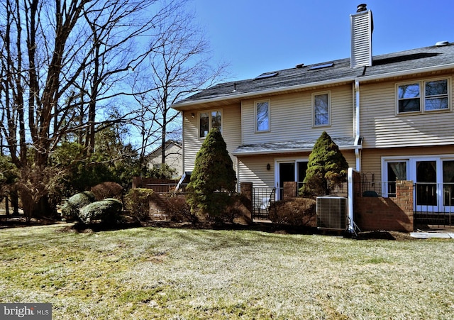 rear view of house with central AC unit, a lawn, and a chimney