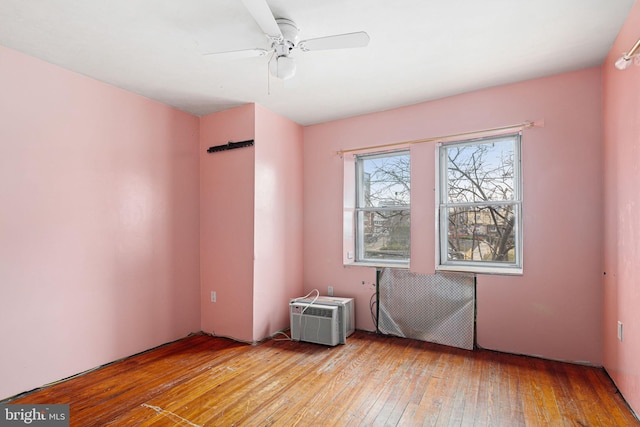 empty room with ceiling fan, light wood-type flooring, and a wall unit AC