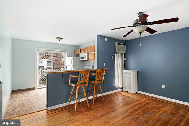 kitchen with ceiling fan, a wall mounted air conditioner, white appliances, a kitchen bar, and light wood-type flooring