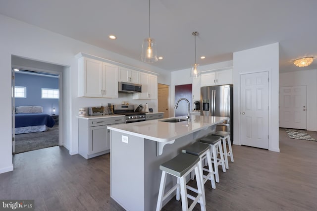 kitchen featuring a center island with sink, hanging light fixtures, sink, appliances with stainless steel finishes, and white cabinetry