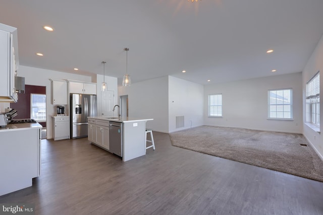 kitchen with a kitchen island with sink, dark wood-type flooring, sink, appliances with stainless steel finishes, and decorative light fixtures