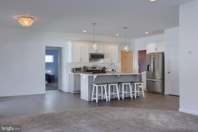 kitchen with a breakfast bar, stainless steel appliances, pendant lighting, white cabinets, and an island with sink