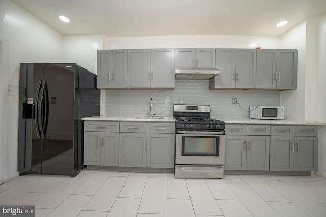 kitchen with gray cabinetry, stainless steel gas stove, black fridge, and sink