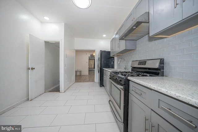 kitchen with ventilation hood, stainless steel gas stove, gray cabinetry, and decorative backsplash