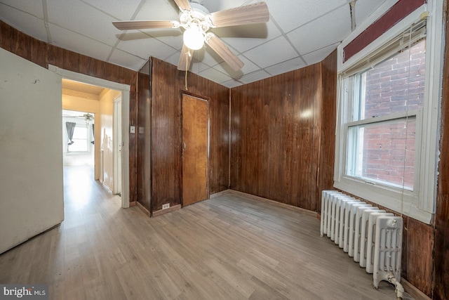 unfurnished room with radiator heating unit, a paneled ceiling, light hardwood / wood-style floors, and plenty of natural light