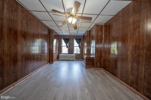 unfurnished room featuring a paneled ceiling, light hardwood / wood-style floors, radiator, and wooden walls